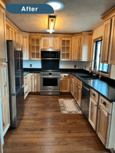 An after picture of a kitchen remodel in Evergreen, showing the entire kitchen with wood cabinets, steel appliances and black countertops.