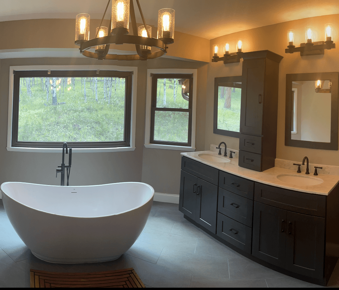 A beautiful bathroom with a deep soaking tub, two sink counter with dark wood finish, and beige tile floor. Mountain scenery is visible through the windows.