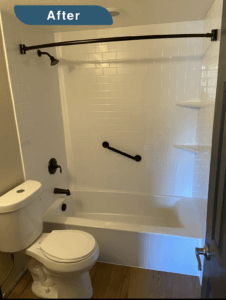 An image labeled "After." A small bathroom with a beautiful bath/shower combo and a toilet. The tile in the shower are white rectangles, and the metal finishes are dark bronze. There is a bar for stability on the shower wall.