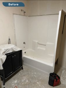 An image labeled "Before." A bathroom in mid construction. There is a single piece unit that contains a bath and shower. The floor is paint spattered concrete. There is a tool bag on the floor and a drop cloth over the sink.